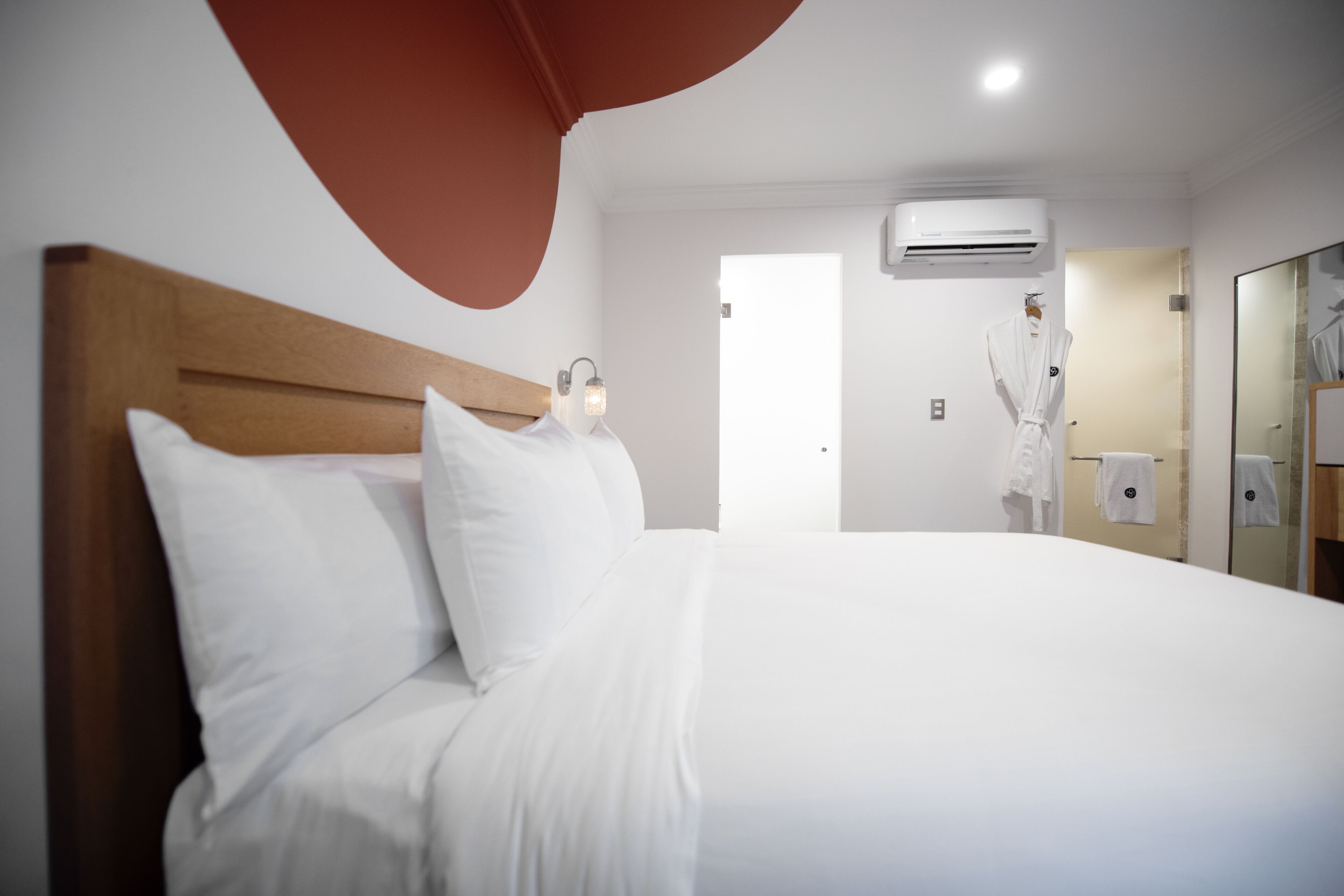 A hotel room with a large bed, an air conditioning unit, a robe hanging on a hook, and a mirror on the wall.
