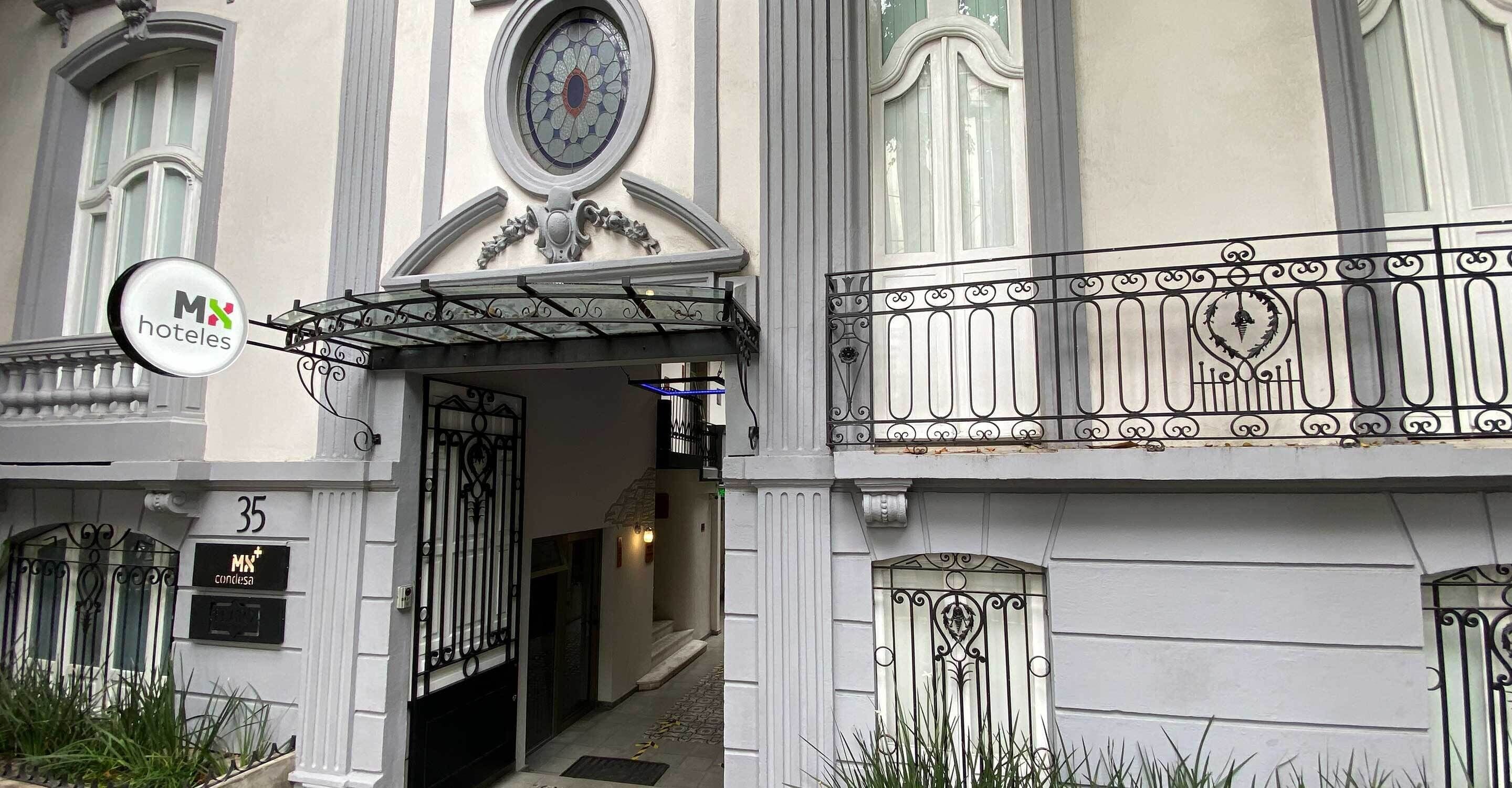 Ein Hotelzugang mit schmiedeeisernem Tor, einem Schild und einem Balkon mit schmiedeeiserner Verzierung.
