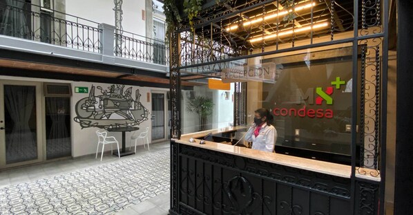 Un espace d’accueil d’hôtel comprenant un comptoir de réception, un réceptionniste et un mur de verre sur lequel est inscrit le nom de l’hôtel.