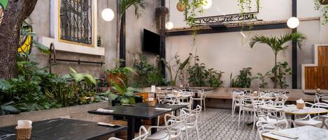 An indoor dining area with tables and chairs, surrounded by various plants and hanging baskets.