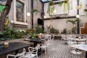 Un'area pranzo interna con tavoli e sedie, circondata da diverse piante e cesti pensili.