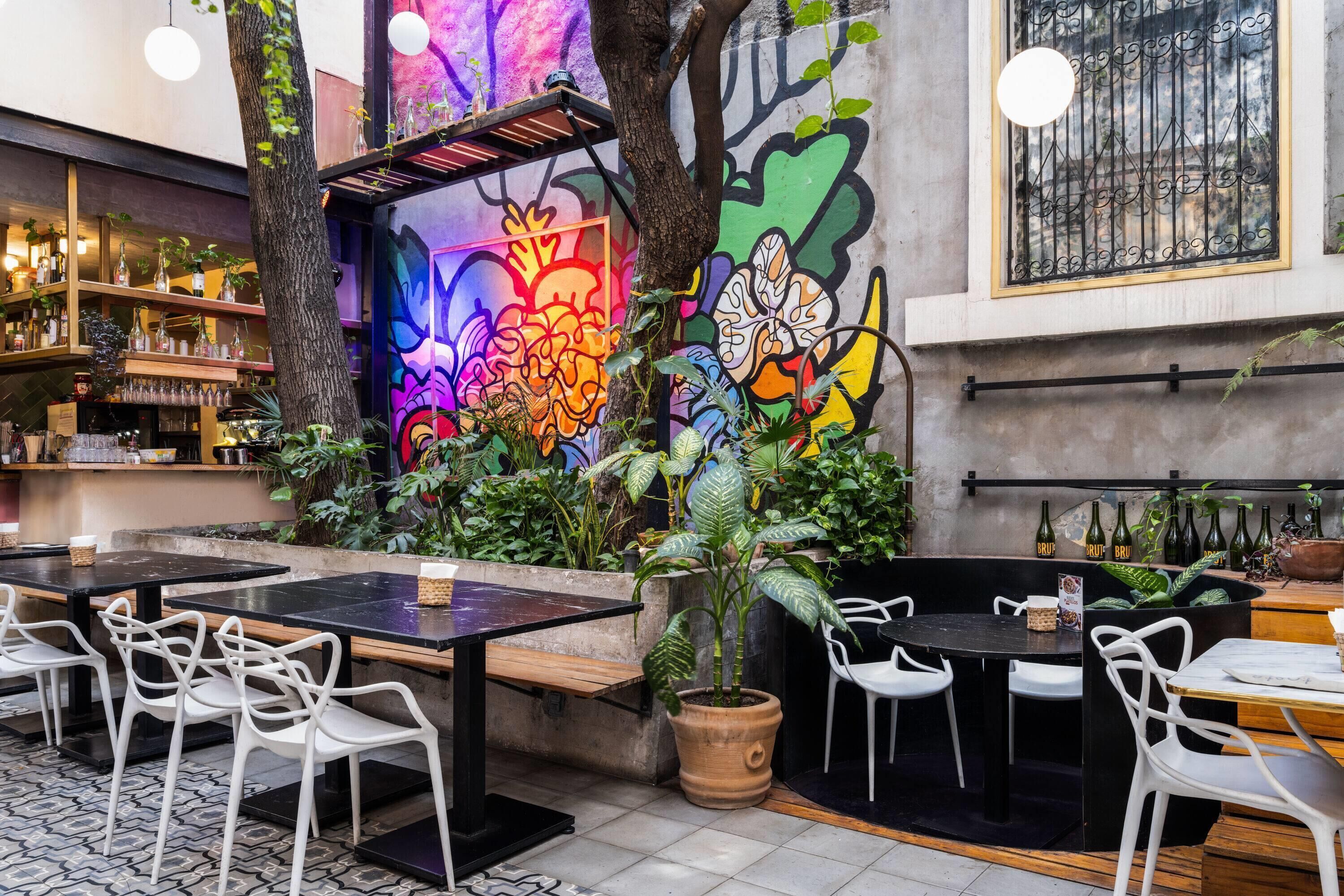 An indoor dining area with tables and chairs, a mural with colorful graffiti, and a variety of plants.