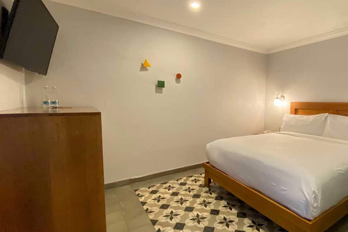 Een hotelkamer met een bed, een houten nachtkastje, een groene accentmuur en een betegelde vloer.