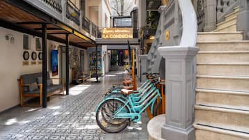 Una calle estrecha con una fila de bicicletas turquesas estacionadas en la acera, una escalera con barandilla blanca y un edificio con un letrero de neón que dice 'LA CONDECHU'.
