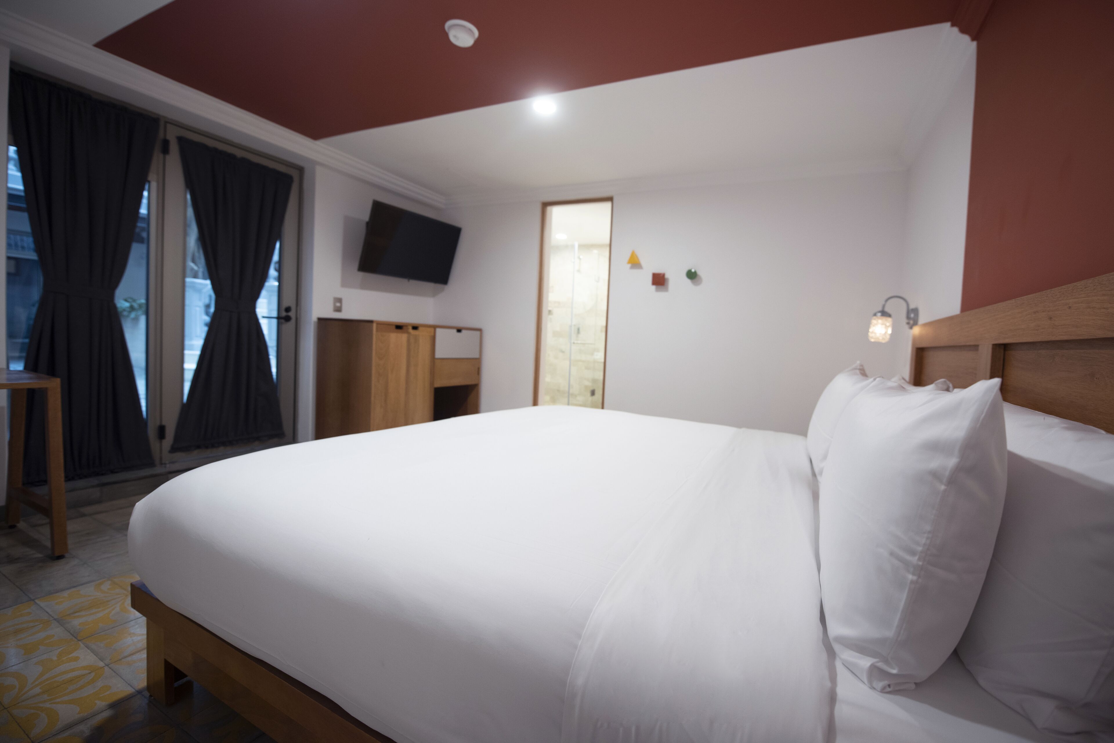 A hotel room with a large bed, a TV mounted on the wall, and a wooden headboard.