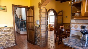 Une cuisine avec une cheminée en pierre, un coin repas avec une table et des chaises en bois, et un escalier menant à un autre niveau.
