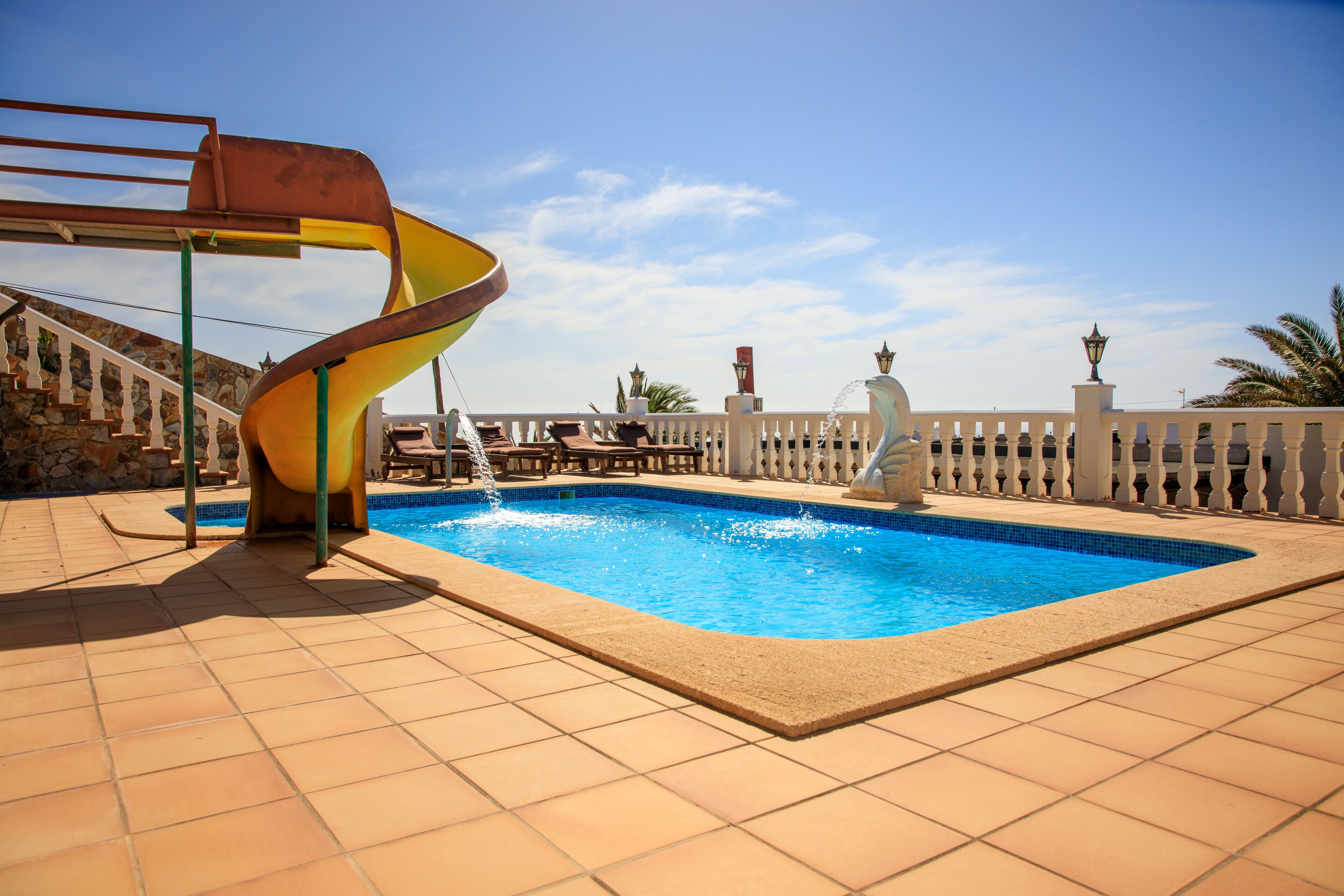 A swimming pool with a spiral slide, a stone wall, and a white fence.