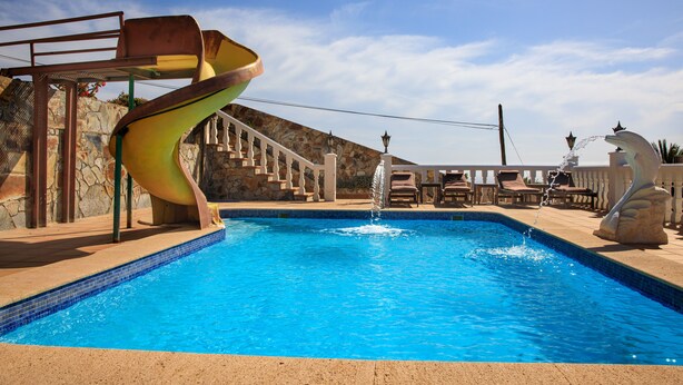 Une piscine avec un toboggan en spirale, un mur en pierre et une fontaine.