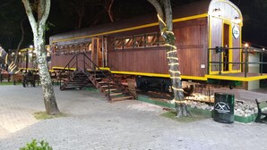 Un vagón de tren estacionado transformado en restaurante con mesas al aire libre y una escalera que lleva a la entrada.