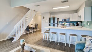 Una cocina moderna con una isla central, taburetes de bar y un comedor con una escalera.