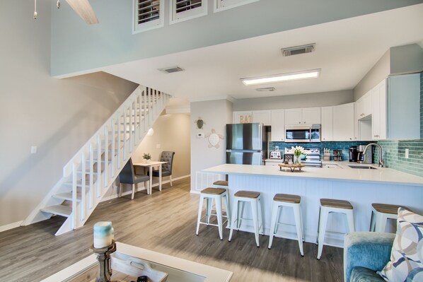 Una cocina moderna con una isla central, taburetes de bar y un comedor con una escalera.