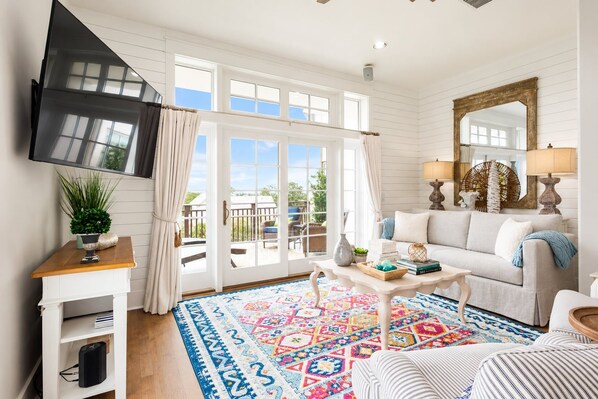 A spacious living room with a large window, a flat-screen TV, a white sofa, a patterned rug, and a wooden coffee table. - Paradise Found on 30A - 2BR Seagrove Condo - Lake and Gulf Views - Golf Cart (Santa Rosa Beach)