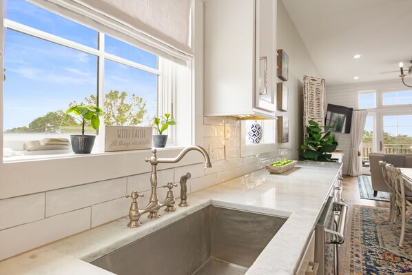 A modern kitchen with a large window, stainless steel sink, and potted plants. - Paradise Found on 30A - 2BR Seagrove Condo - Lake and Gulf Views - Golf Cart (Santa Rosa Beach)