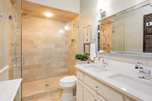 Une salle de bain moderne avec une douche en verre, des toilettes blanches et un grand miroir au-dessus du lavabo.