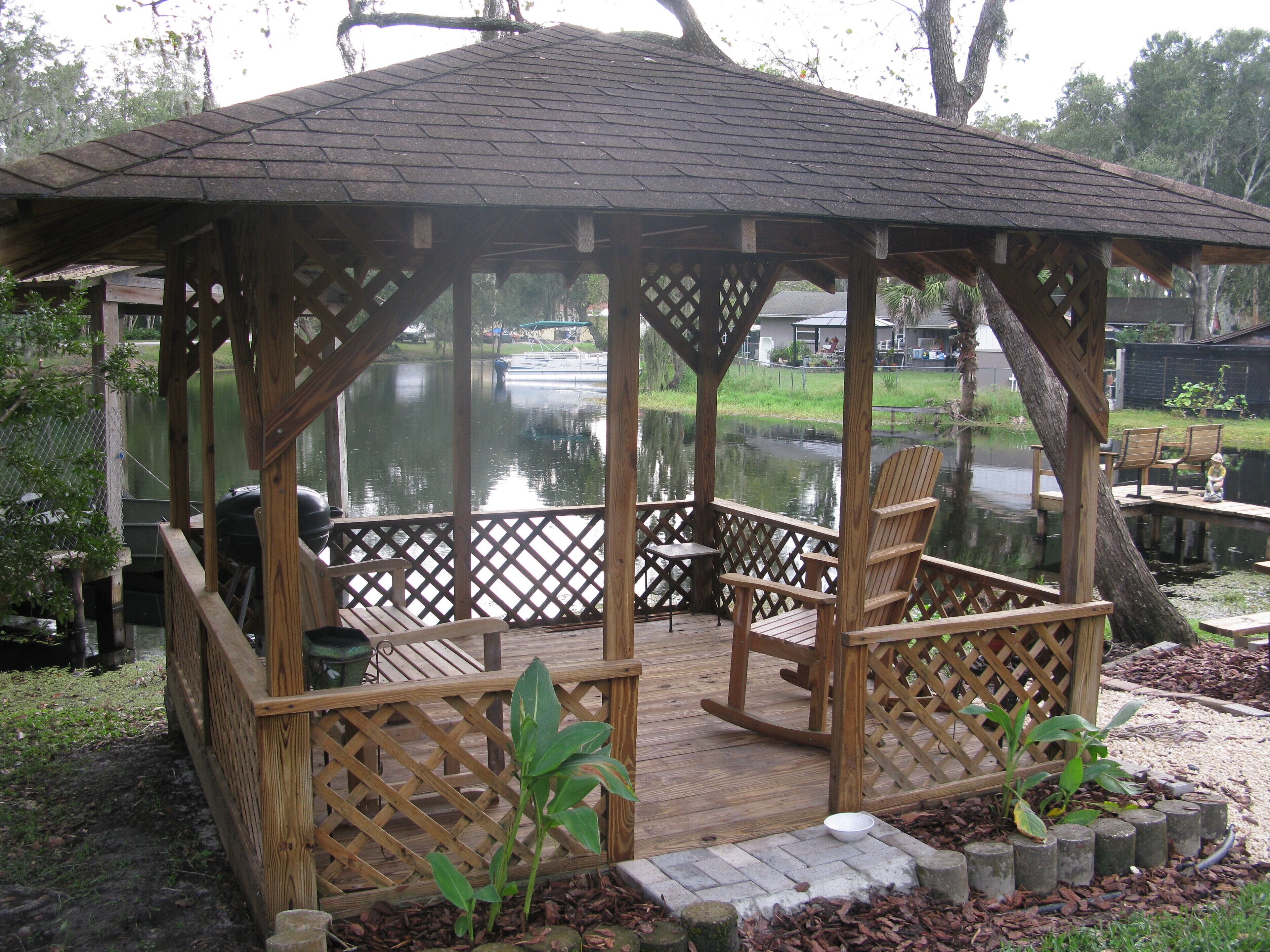 Ein hölzernes Pavillon mit Gitterboden, umgeben von einem Teich und Bänken.
