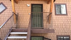 Un immeuble de deux étages avec une porte verte, un balcon et un escalier.