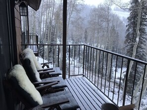 A wooden deck with benches covered in snow, overlooking a snowy forest.