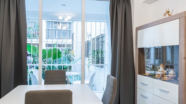 A modern dining area with a white table and chairs, a large window with curtains, and a view of a balcony with plants and outdoor furniture. - El Rincón de Maria y Pedro (Torremolinos)