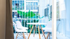 A modern indoor space with a white table and chairs, large windows, and a view of a building with balconies and greenery. - El Rincón de Maria y Pedro (Torremolinos)