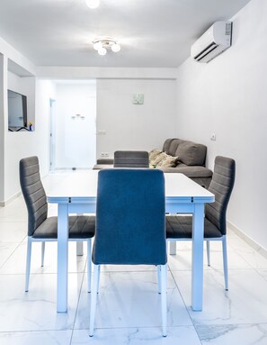 A modern dining area with a white table and four grey chairs, a grey sofa, and a ceiling light fixture. - El Rincón de Maria y Pedro (Torremolinos)