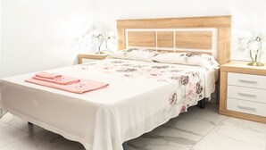 A neatly made bed with a floral bedspread, a pair of pink towels, and a wooden headboard. - El Rincón de Maria y Pedro (Torremolinos)