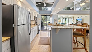 A modern kitchen with a stainless steel refrigerator, white cabinets, and a large island with a marble countertop. - SeaPines, Remodeled, Lovely Golf View, Pet Friendly (Hilton Head Island)
