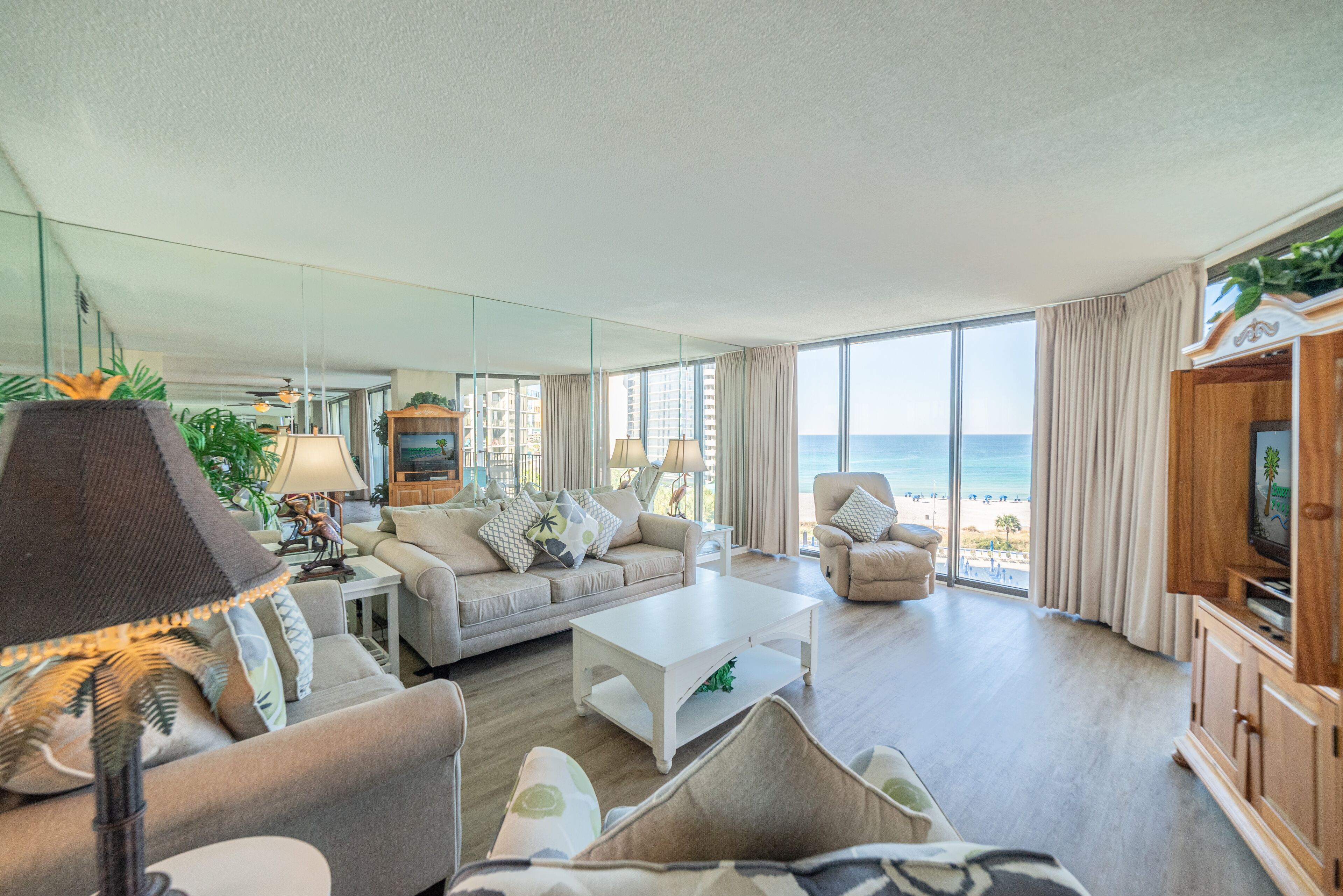 Een ruime woonkamer met een groot raam met uitzicht op een strand, ingericht met een bank, fauteuils en een salontafel.