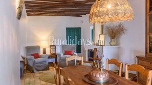 A cozy living room with a wooden dining table, two armchairs, a sofa, and a decorative lamp.