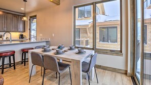 A modern kitchen with a large dining table, bar stools, and a view of a snowy outdoor area through large windows. - Relax Fireside: Silverthorne Home 11 Mi to Skiing! (Silverthorne)