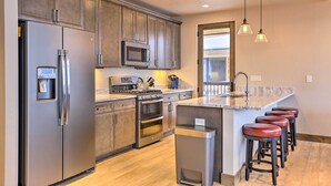 A modern kitchen with stainless steel appliances, wooden cabinets, a microwave, and a built-in oven. There are bar stools and a large window providing natural light. - Relax Fireside: Silverthorne Home 11 Mi to Skiing! (Silverthorne)