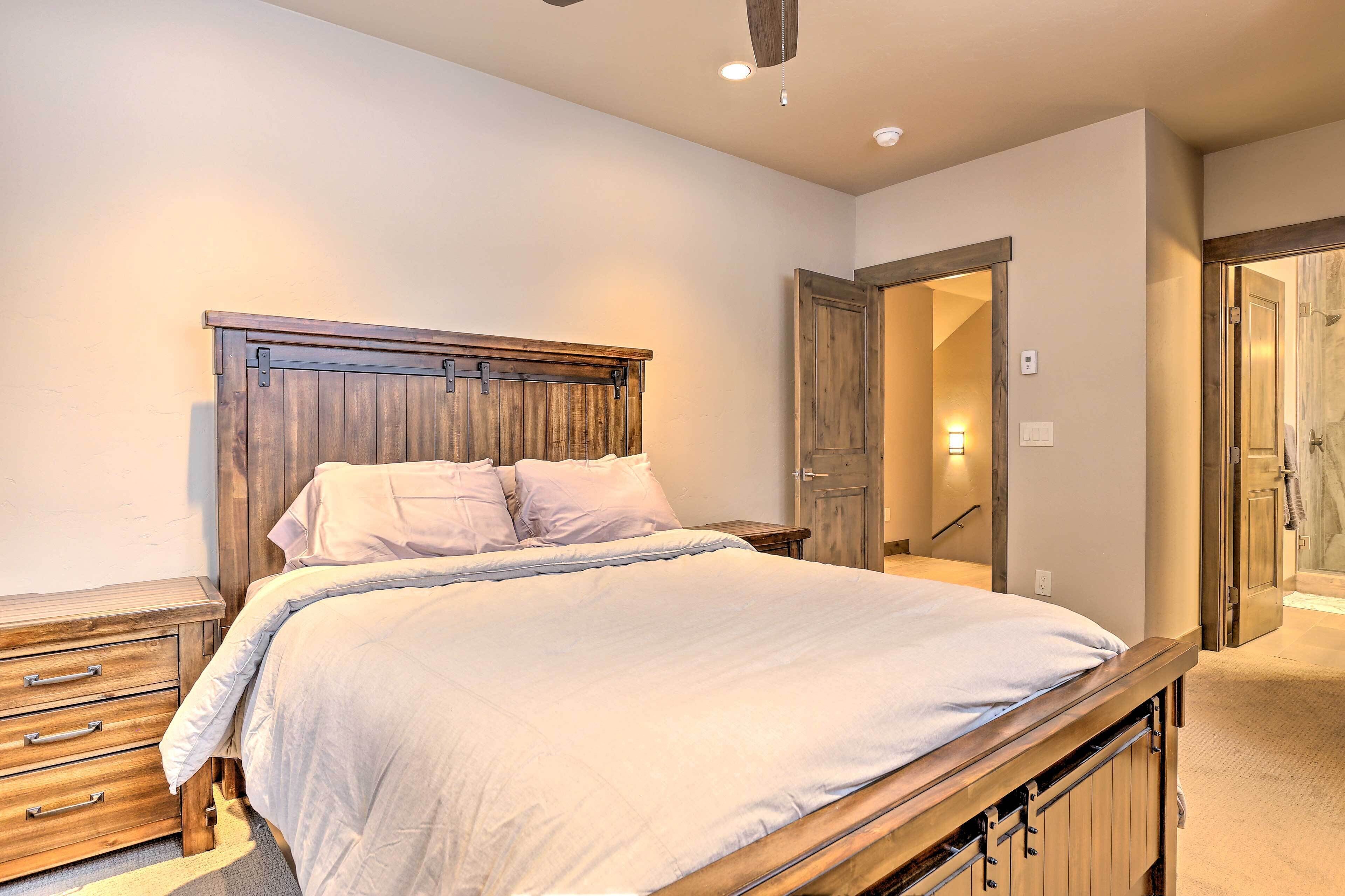 Een slaapkamer met een houten bedframe, een nachtkastje en een dressoir. Er is een deur die naar een andere kamer leidt.