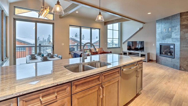 A modern kitchen with a large island, double sinks, and a built-in oven. There are large windows providing natural light and views of the outside. - Relax Fireside: Silverthorne Home 11 Mi to Skiing! (Silverthorne)
