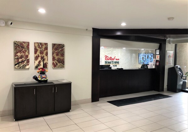 Una recepción con un cartel de Red Roof Inn, un mueble negro con un jarrón decorativo y tres cuadros abstractos en la pared.