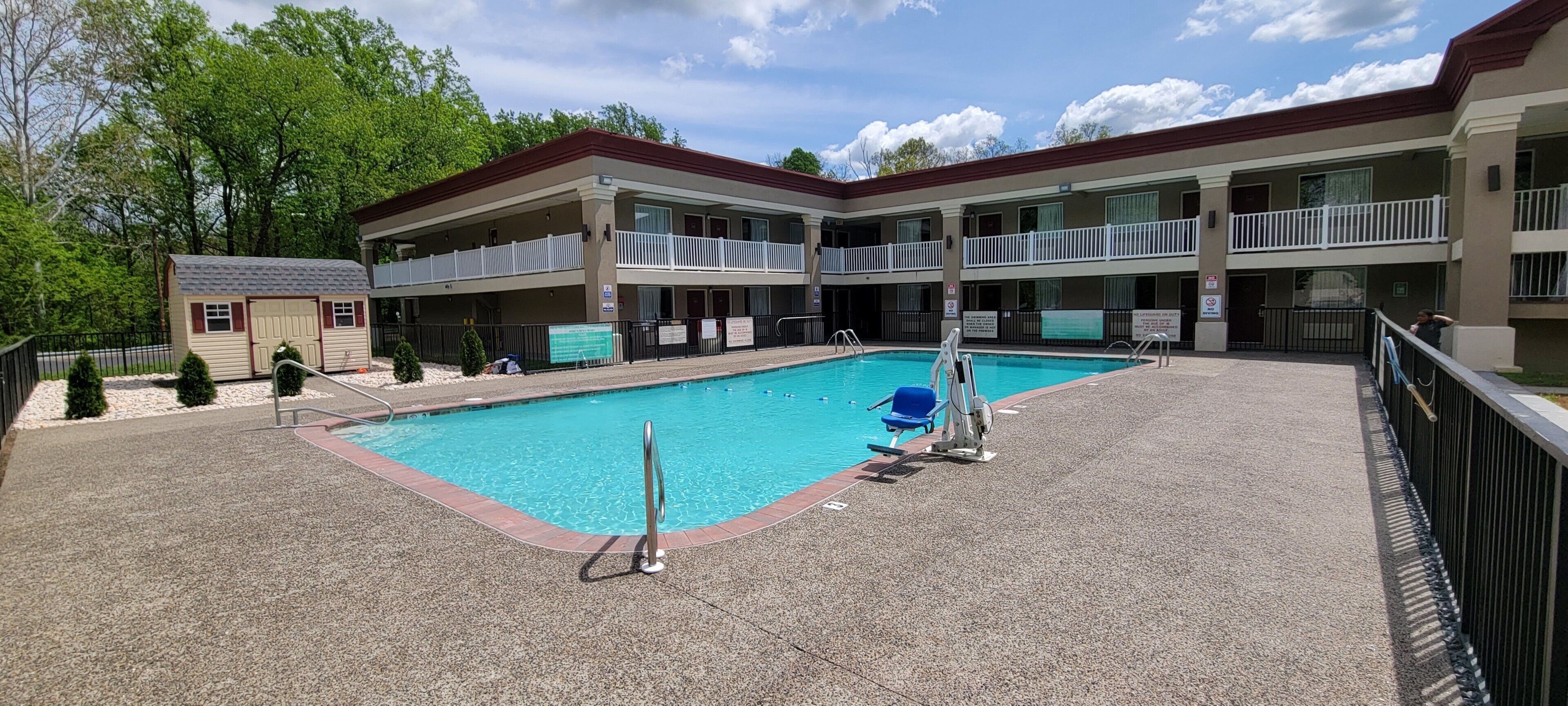 A hotel with a swimming pool, multiple balconies, and a small building to the left.
