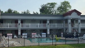 A multi-story motel with a swimming pool, a fenced parking area, and a balcony on the upper floor. - HomeTowne Studios by Red Roof Bordentown - McGuire AFB (Bordentown)