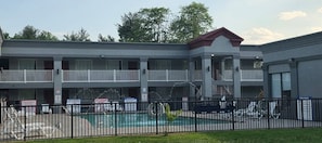Ett flervåningsmotell med en swimmingpool, en inhägnad parkeringsplats och en balkong på översta våningen.