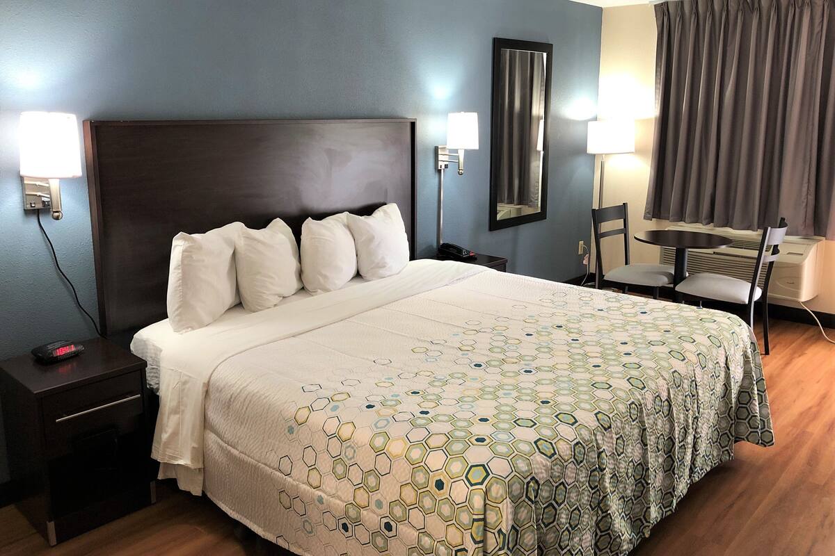 Een hotelkamer met een groot bed, een nachtkastje met een lamp, een stoel, een tafel en een spiegel aan de muur.