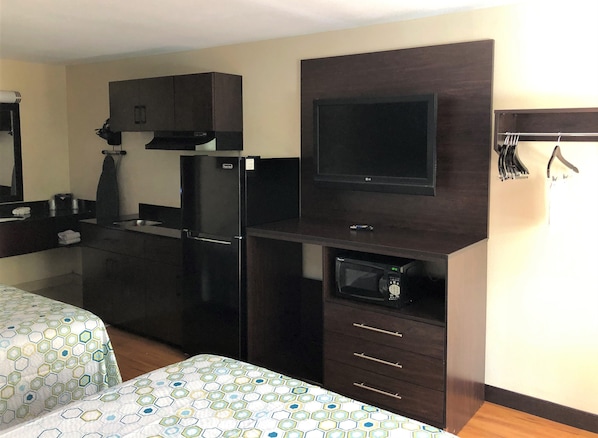 Quarto de hotel compacto com cozinha compacta, televisão de tela plana, micro-ondas e uma cama com colcha estampada.