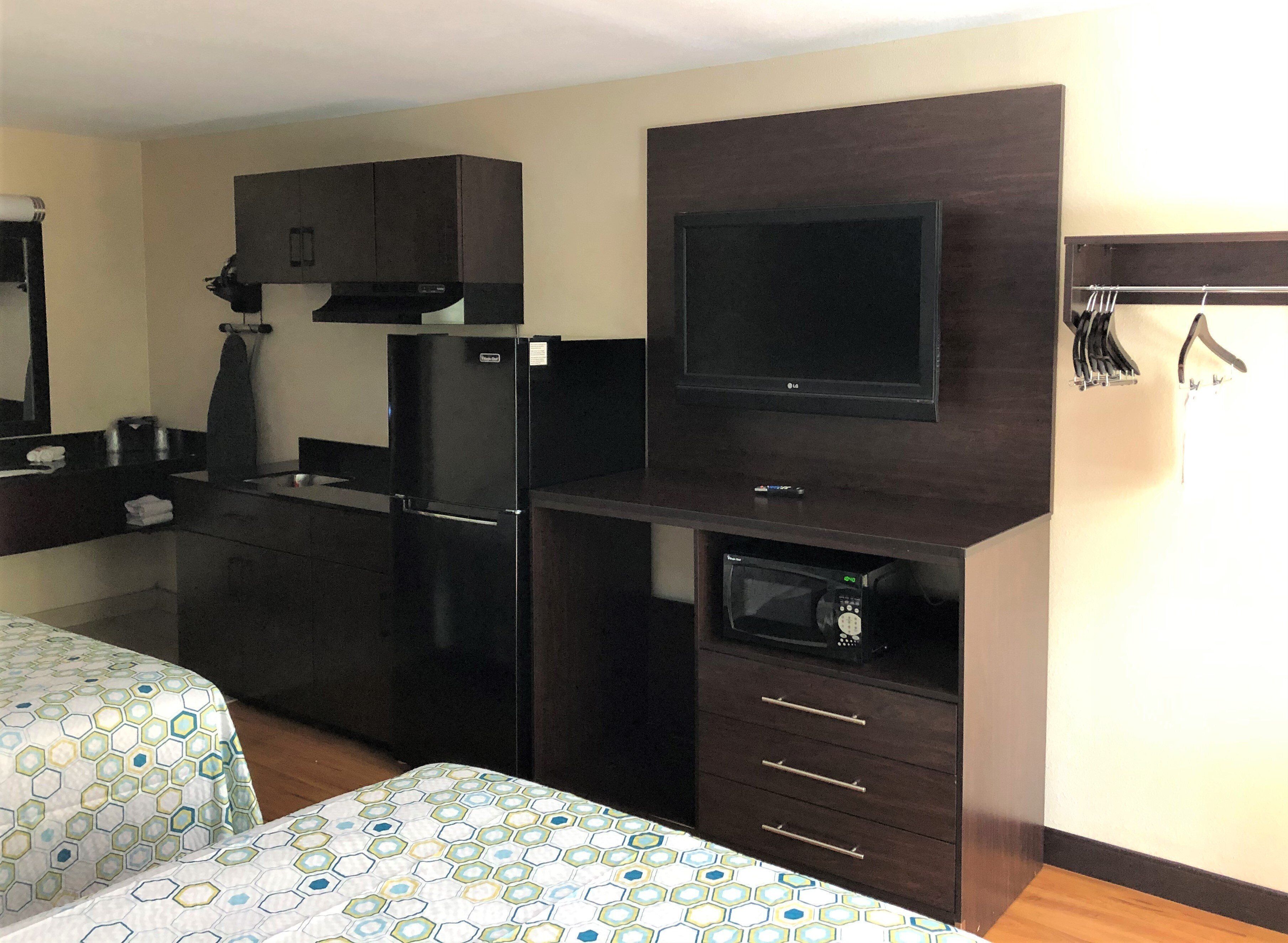 A hotel room with a kitchenette, a flat-screen TV, a microwave, and a bed with a patterned bedspread.