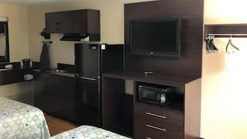 A hotel room with a kitchenette, a flat-screen TV, a microwave, and a bed with a patterned bedspread.