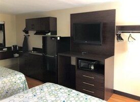 Habitación de hotel con kitchenette, televisor de pantalla plana, microondas y cama con colcha estampada.