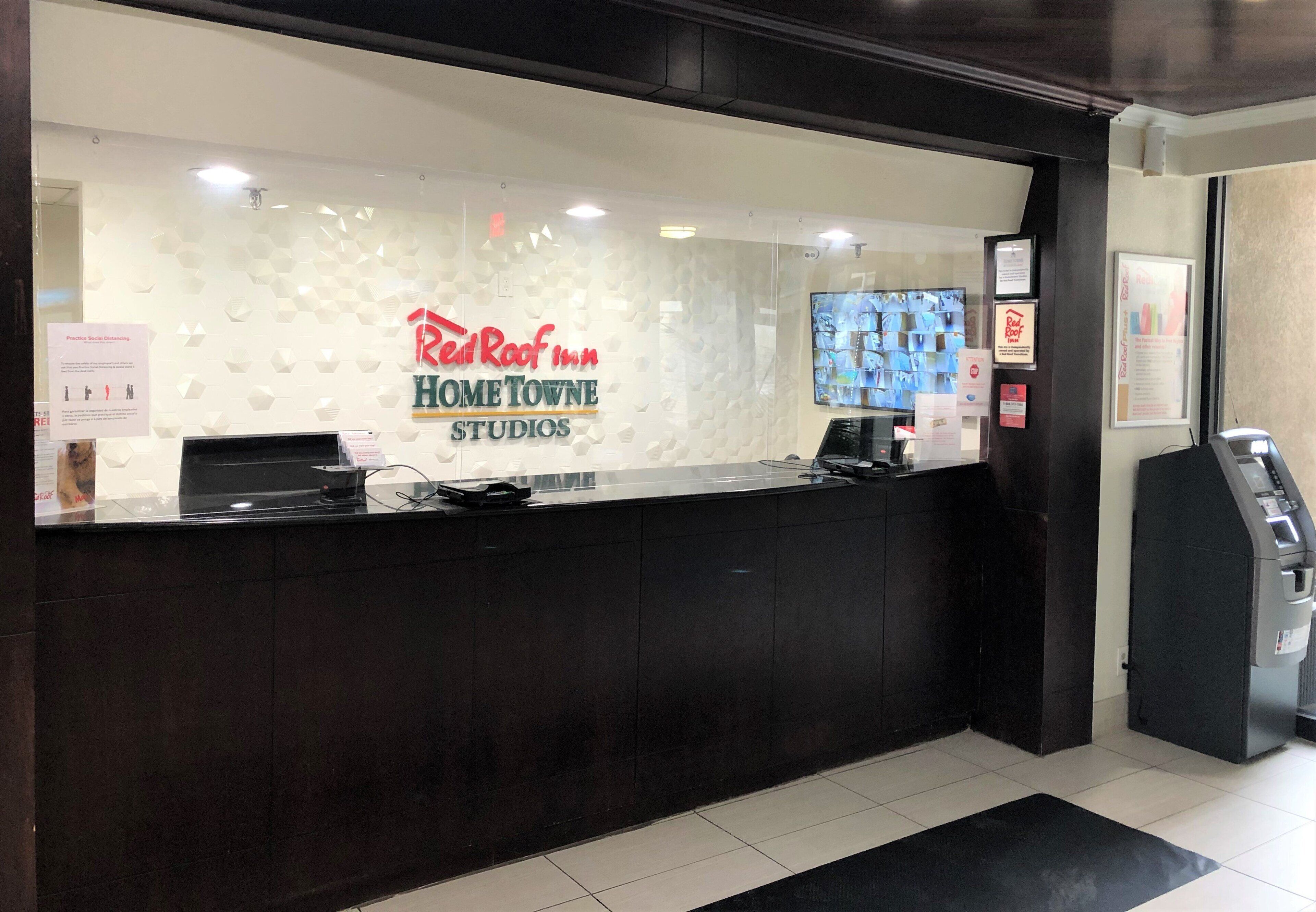 Un mostrador de recepción con una partición de vidrio, una pantalla digital y el letrero de Red Roof Inn.