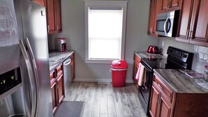 A kitchen with wooden cabinets, a stainless steel refrigerator, a microwave, a stove, and a red trash bin. - Serene, Modern, Cottage, access to a 60 Acre Lake  (Potosi)
