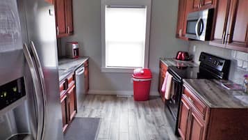 A kitchen with wooden cabinets, a stainless steel refrigerator, a microwave, a stove, and a red trash bin.