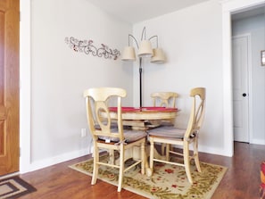 Un coin repas comprenant une table ronde, quatre chaises, un tapis à motifs floraux et un luminaire fixé au mur.