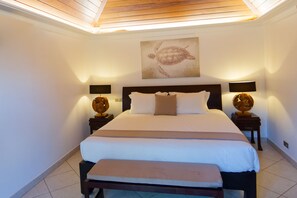 Une chambre à coucher avec un grand lit, deux tables de chevet avec des lampes, un luminaire au plafond et une œuvre d’art représentant une tortue, accrochée au mur.