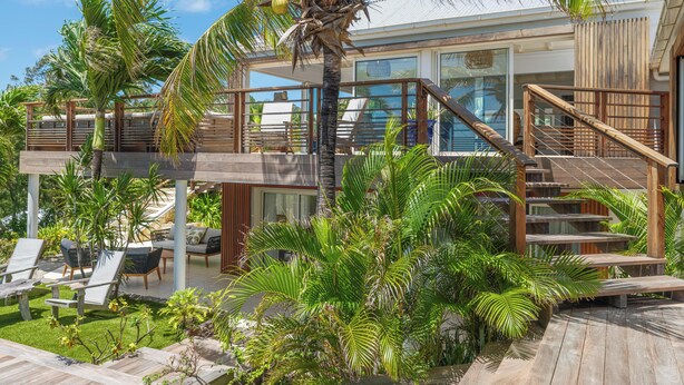 Een modern huis met een houten terras, zitplaatsen buiten en een trap naar een balkon.