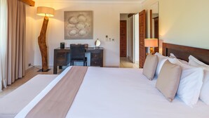 Een hotelkamer met een houten plafond, een groot bed met witte lakens, een bureau met een stoel en een wandlamp.