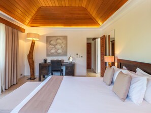 Habitación de hotel con techo de madera, una cama grande con ropa blanca, un escritorio con silla y una lámpara fijada a la pared.