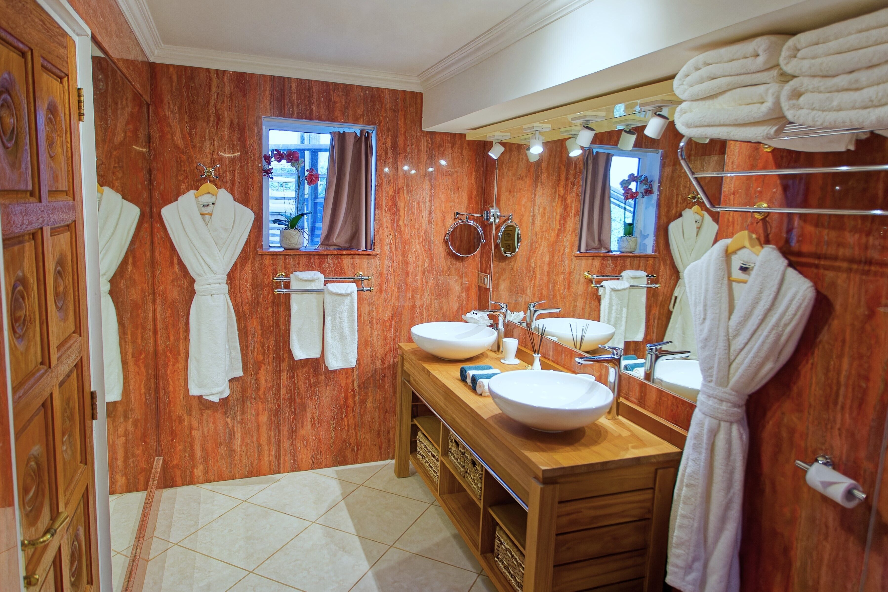 Une salle de bain avec des murs en bois, deux lavabos, un grand miroir et des serviettes rangées sur des étagères.